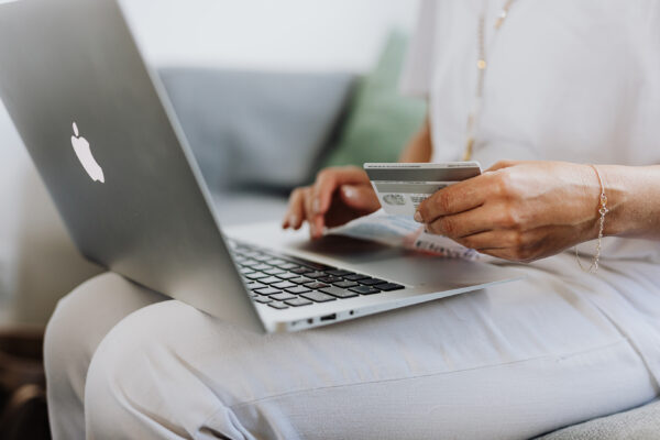 kobieta dokonująca zakupów online trzymająca na kolanach macbooka a w dłoni kartę kredytową